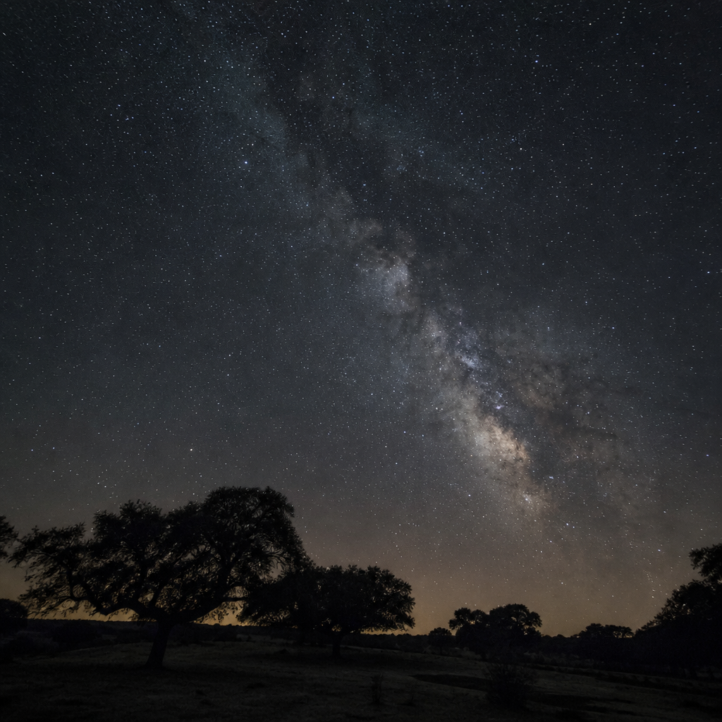 Cielo estrellado de la Reserva Starlight de Los Pedroches sobre siluetas de encinas en Hinojosa del Duque
